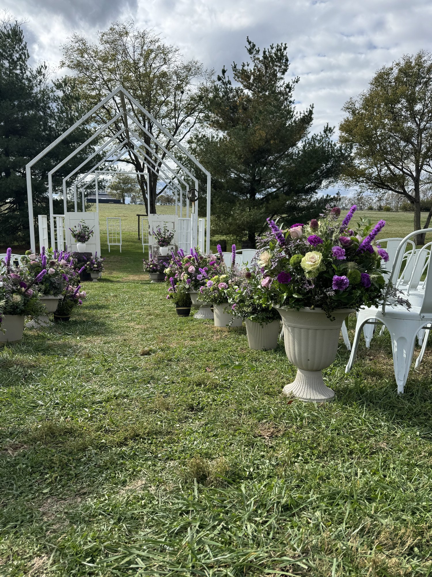 Urns of purple and lavender flowers along a ceremony aisle