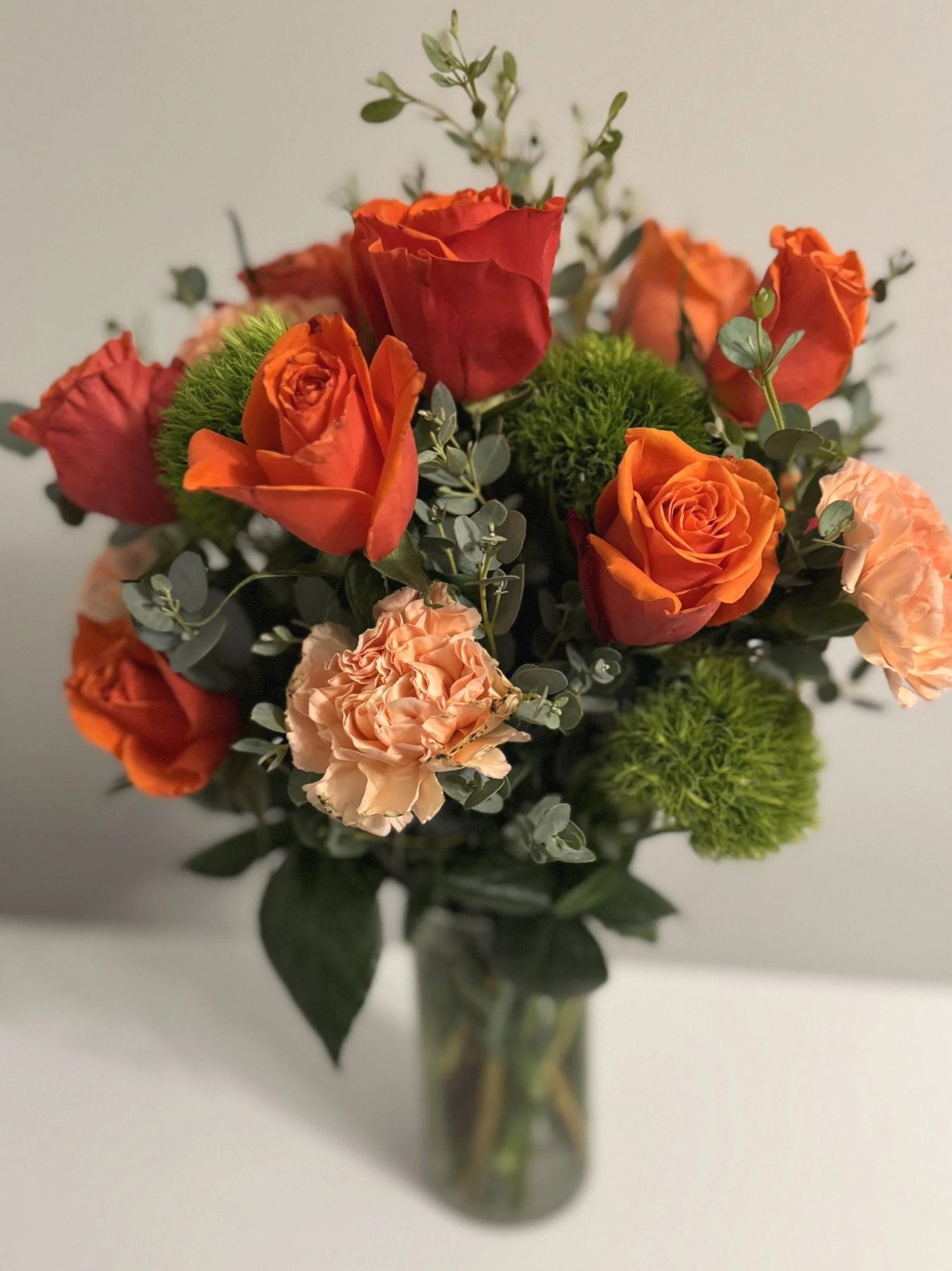 Orange roses and peach carnations with eucalyptus in a glass vase